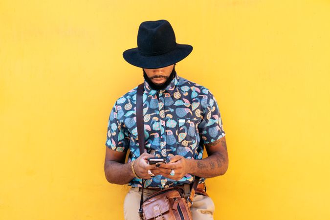 Stylish Black man using smartphone outdoors over yellow background
