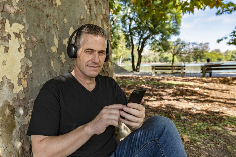Man listening to music, sitting on the grass, and leaning on a tree
