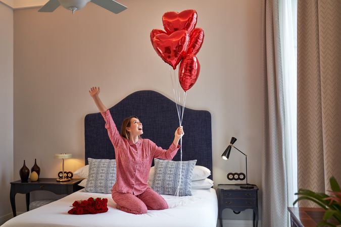 Cheerful woman on bed with bunch of red heart balloons