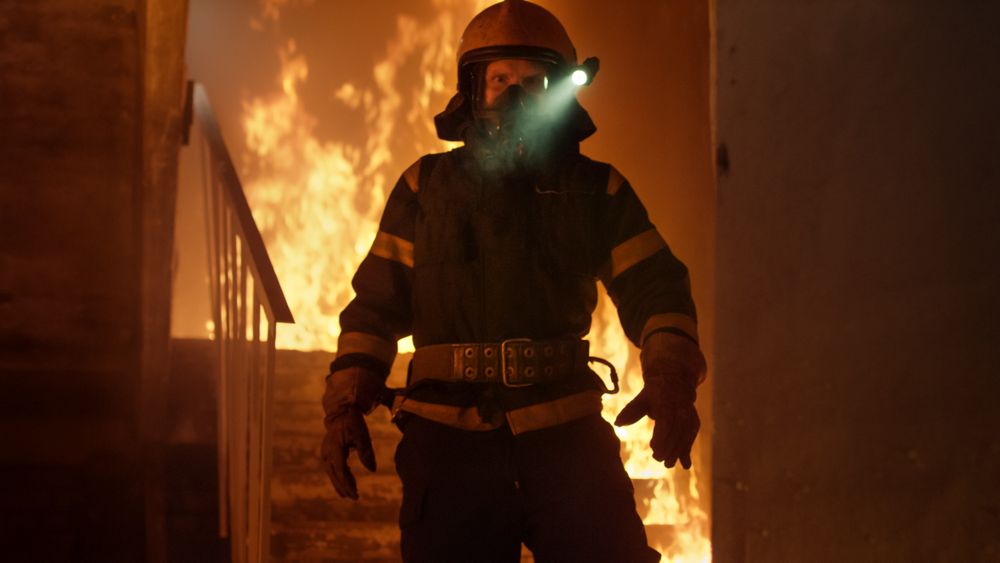 Firefighter with flashlight on helmet standing alone in burning staircase