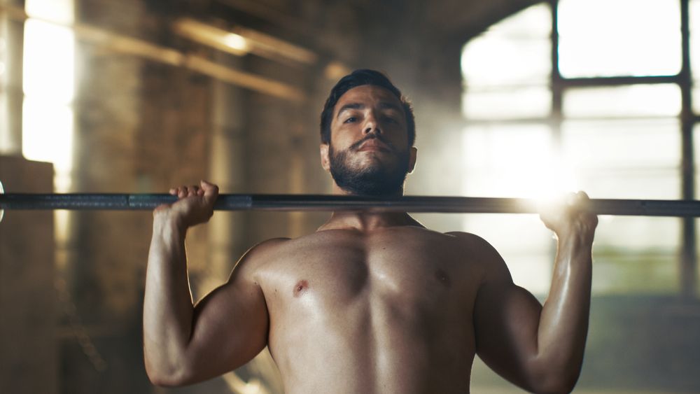 Close-up of a Muscular Shirtless Man Lifting Heavy Barbell and Doing Military Press Exercise in the Industrial Gym Building.