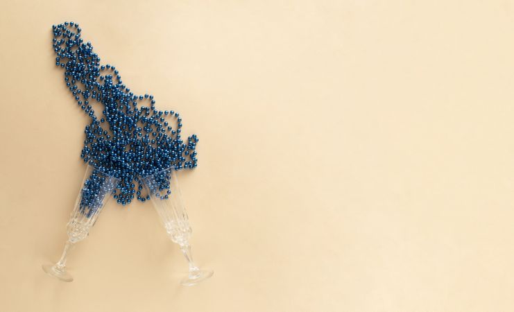 Two champagne glasses on a beige table with blue beads copy space