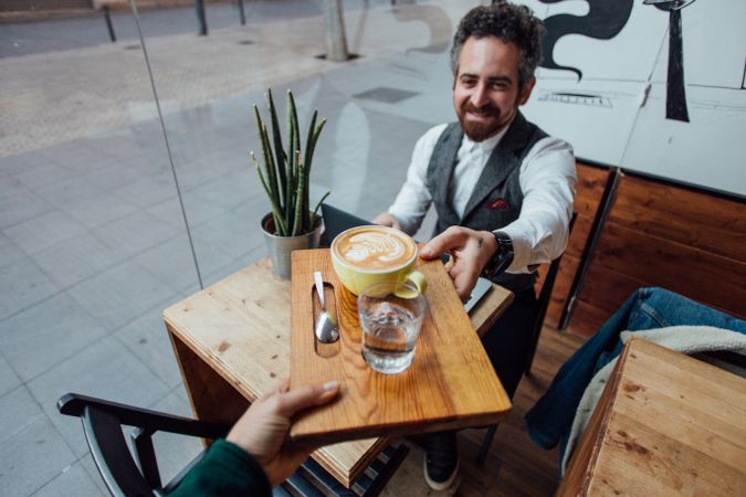 Waiter serves man coffee with latte art