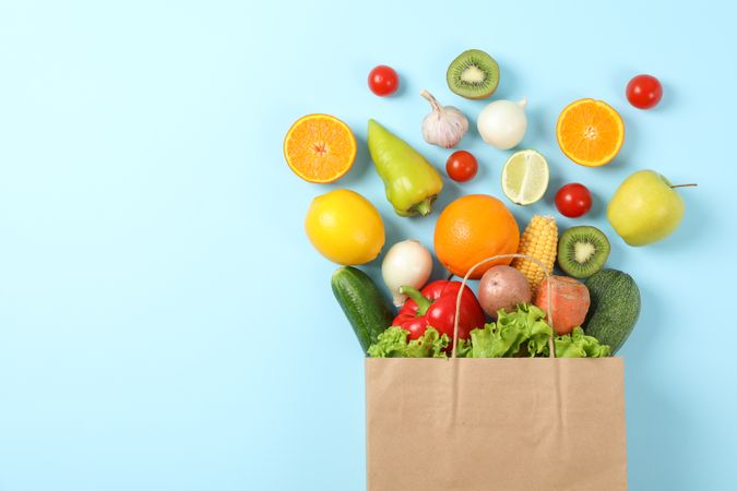 Flat lay with paper bag, vegetables and fruits on blue background, copy space