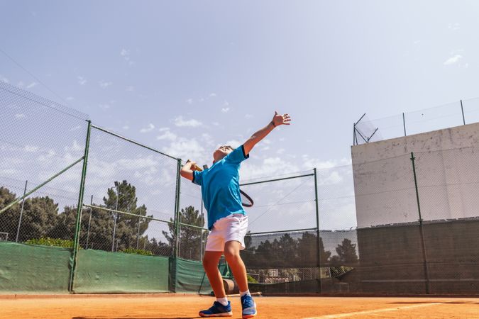 Little boy playing tennis on a dirt court making a serve