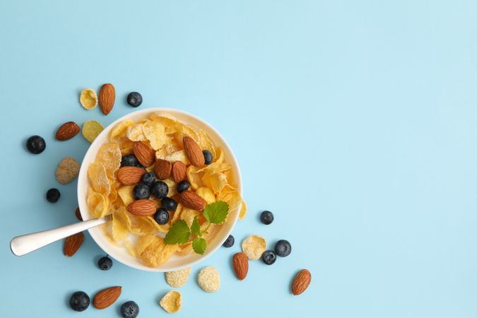 Bowl with muesli, almond, mint and blueberry on blue background