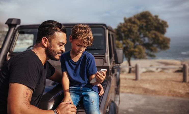 Father and son in front of car using mobile phone