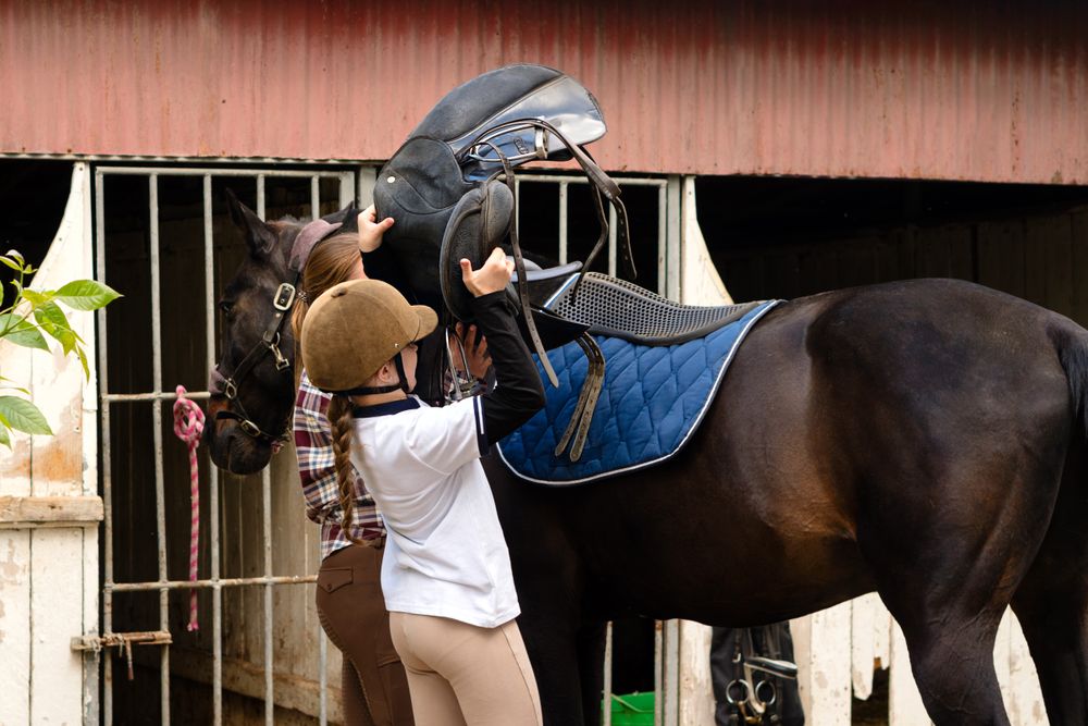 Instructor and girl placing saddle on horse