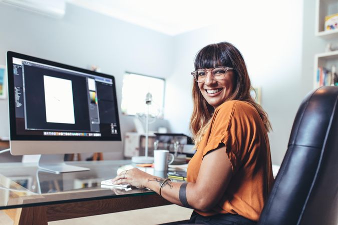 Cheerful illustrator sitting at her desk looking back and smiling at camera