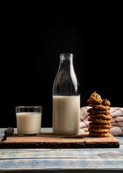 Milk and fresh cookies on board near napkin