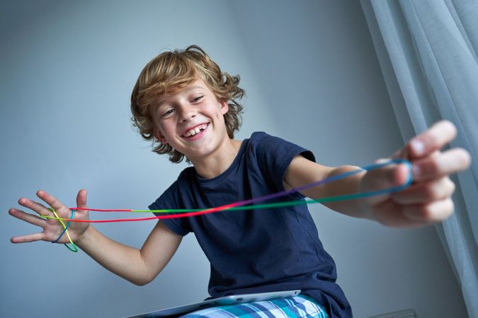 Cheerful boy playing string game in living room