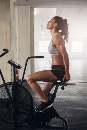 Side view shot of fitness woman spinning air bike at the gym