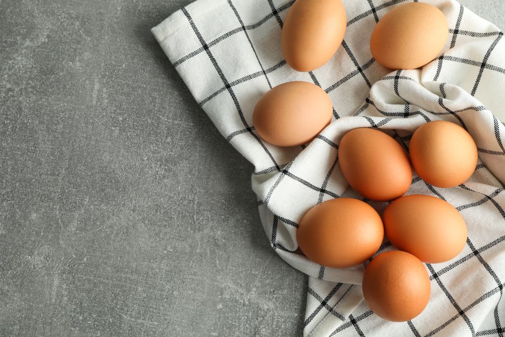 Chicken eggs in kitchen towel on gray background, space for text