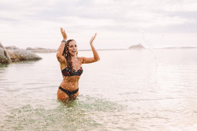 Smiling woman in bikini splashing water and enjoying the ocean water