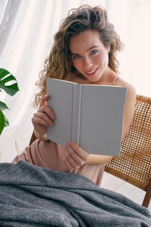 Smiling woman sitting with book on chair