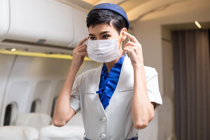 Flight attendant putting on facemask in airplane