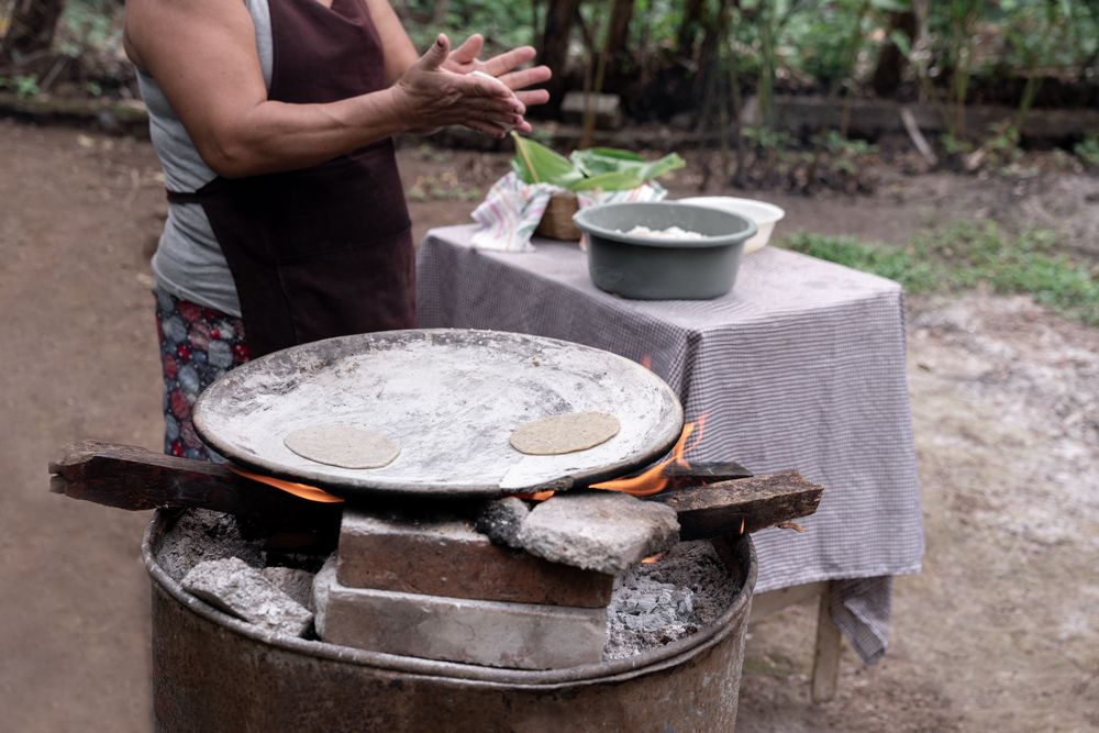 An adult Hispanic woman is shaping corn tortillas by hand