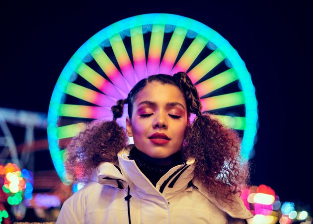 Close up of young woman’s face in front of Ferris wheel lit at night