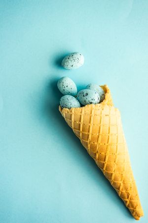 Waffle cone with blue speckled eggs on blue pastel background