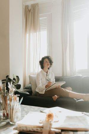 Woman writing on paper on sofa in room