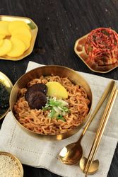 Brass pot full of noodles with radish, onion and mushroom garnish with side of kimchi