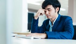 Frustrated Asian male in suit working at computer in his office