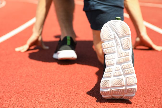 Sportsman low starting to run on red athletic track, close up