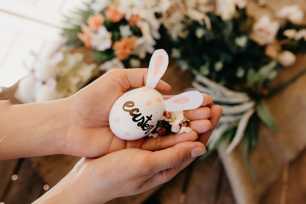 young woman holding an easter egg with rabbit ears painted by children with flowers