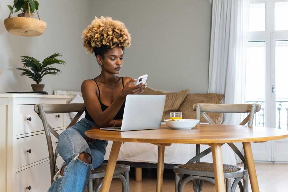 Black woman with laptop and mobile phone sitting on chair during breakfast