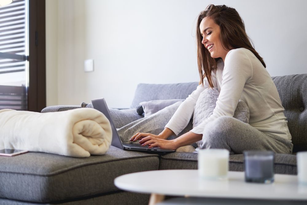 Smiling woman browsing on laptop and sitting on settee