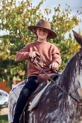 Boy in hat riding his brown mottled horse