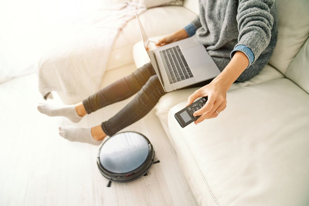Person sitting with laptop on sofa and switching remote control