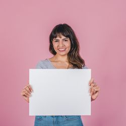 Smiling woman holding a blank sign against a pink background