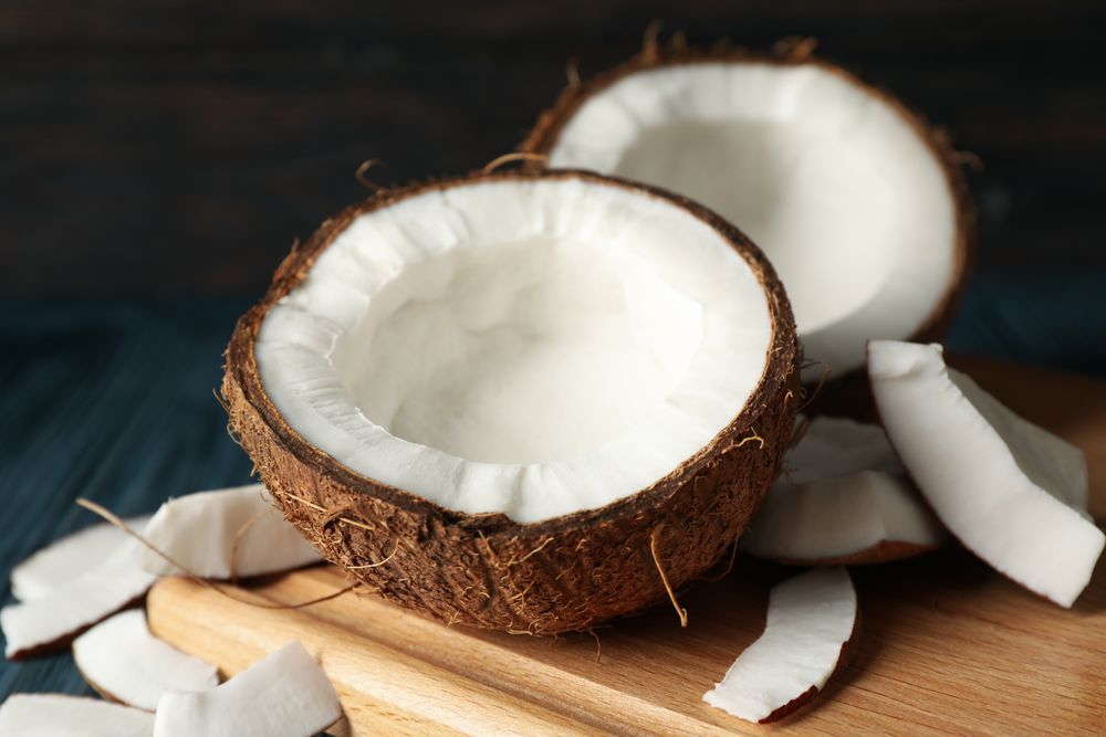 Board with coconut on wooden background, close up