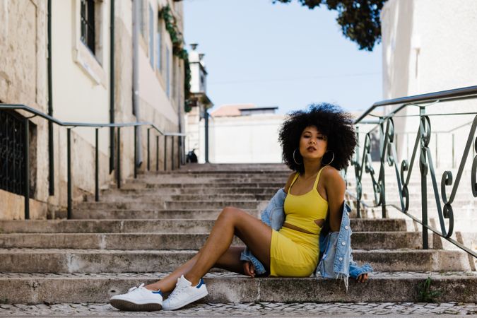 Stylish Black female sitting in stairs with railing outdoors