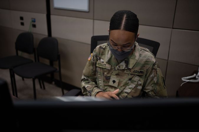 US female soldier with facemask working on her desk in office
