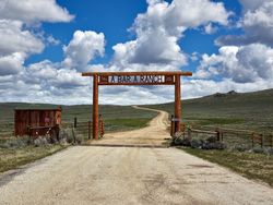 Ranch gate stop a rural road against blue cloudy sky outside Riverside, Wyoming bDjEp5