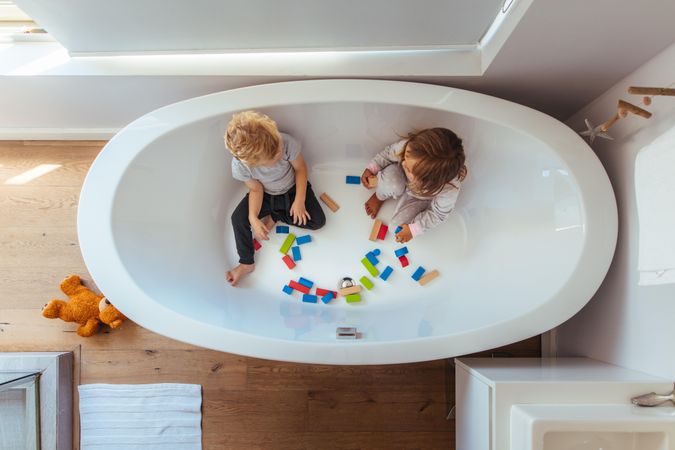 View of above of siblings sitting in an empty bathtub with wooden blocks