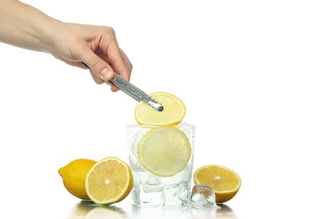 Hand holding tongs putting lemon slice in rocks glass full of ice