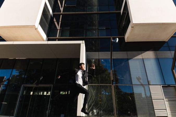 Businessman jumping against glass office building