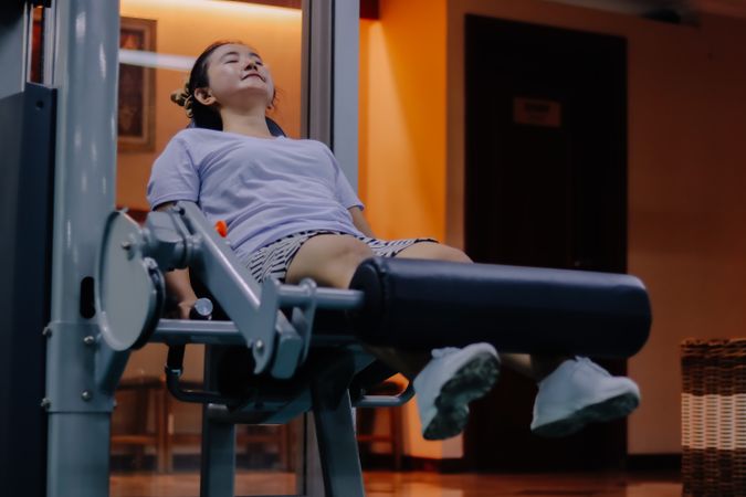 woman wearing purple shirt, shorts, and white shoes, is using a leg extension exercise machine.