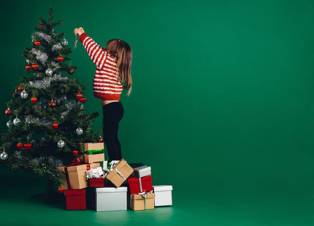 Little girl decorating a Christmas tree standing on gift boxes