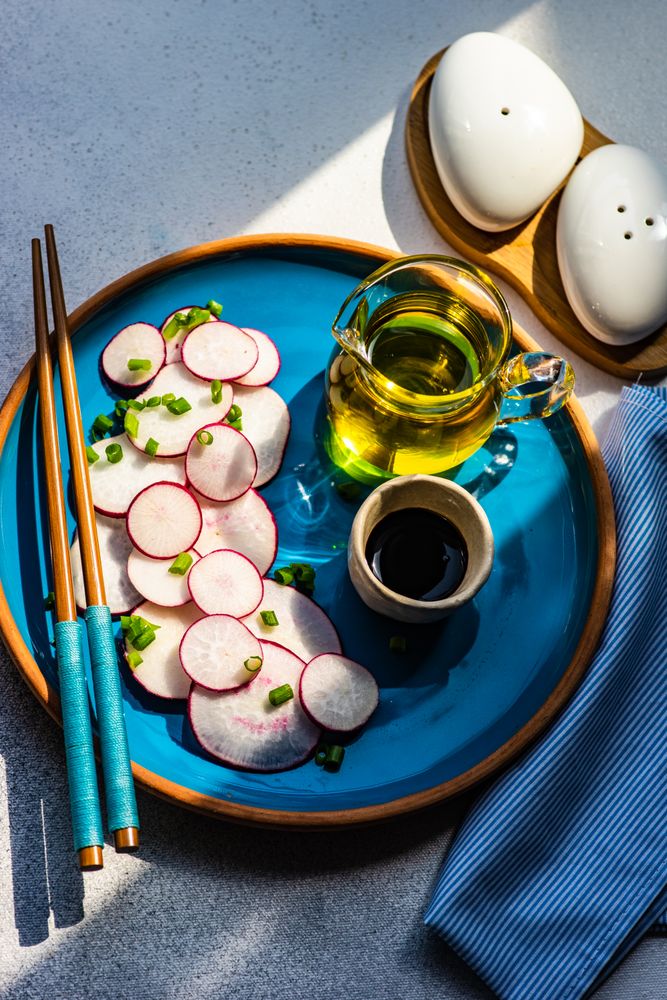 Top view of sliced radishes on blue plate served with oil and chopsticks