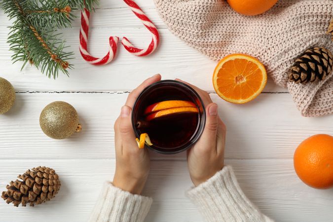 Girl holding glass with mulled wine on decorated wooden background, top view
