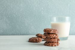 Stack of chocolate cookies with glass of milk on table against light background