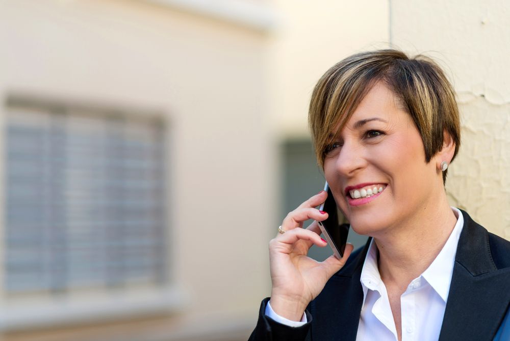 Portrait of smiling woman wearing a blazer and speaking on phone outside