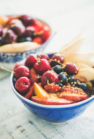 Blue bowl of fresh fruit with cherries, peaches, blueberry with honey