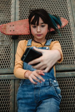 Girl with smartphone and skateboard lying on walkway
