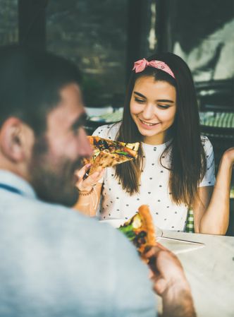 Couple eating pizza al fresco with wine, both smiling