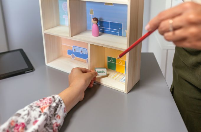 Unrecognizable teacher teaching recycling with a toy house to a female student in an ecology classroom